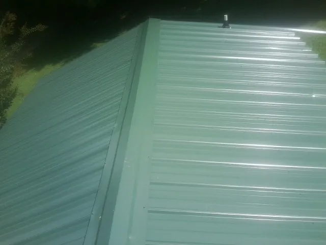 New green metal panels meeting at the ridge of a roof — Flat Roof Repair work by our crew in Pulaski
